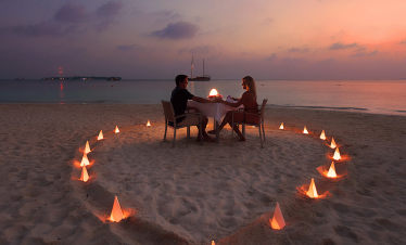 A love-themed candle glowing on a sandy beach, with the ocean in the background.