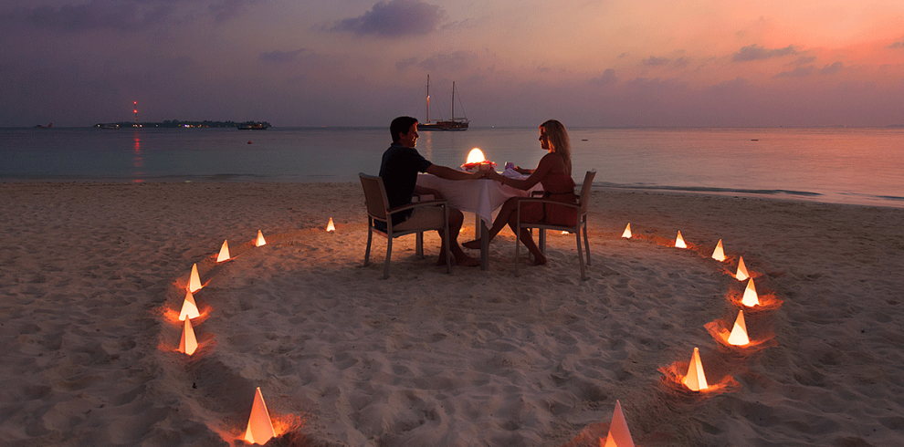 A love-themed candle glowing on a sandy beach, with the ocean in the background.