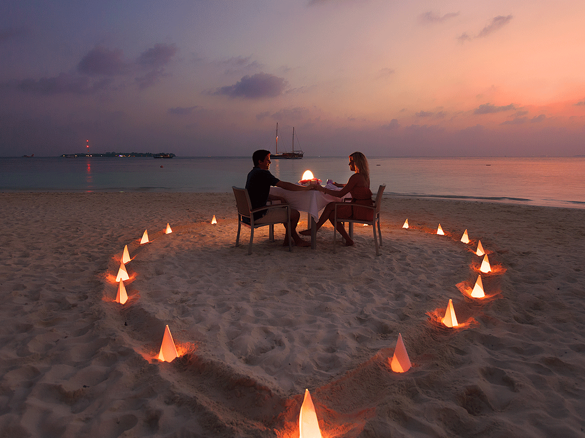 A love-themed candle glowing on a sandy beach, with the ocean in the background.