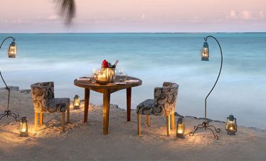 Two chairs and a table surrounded by beautiful lights set up on the beach, creating a cozy and inviting atmosphere.