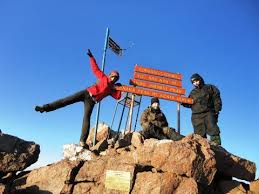 Tourists holding a banner that reads "Congratulations on reaching an altitude of 4,995 meters" on Mount Kenya, celebrating their achievement.