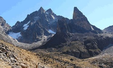 A panoramic view of Mount Kenya, showcasing its rugged, snow-capped peaks against a clear blue sky.