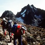 wo tourists climbing Mount Kenya with the assistance of one guide, navigating rocky terrain.