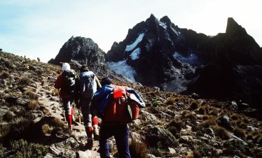 wo tourists climbing Mount Kenya with the assistance of one guide, navigating rocky terrain.