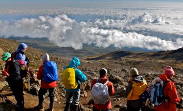 Tourists on Mount Kilimanjaro looking out over a sea of clouds from a high vantage point.