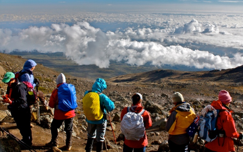 Tourists on Mount Kilimanjaro looking out over a sea of clouds from a high vantage point.