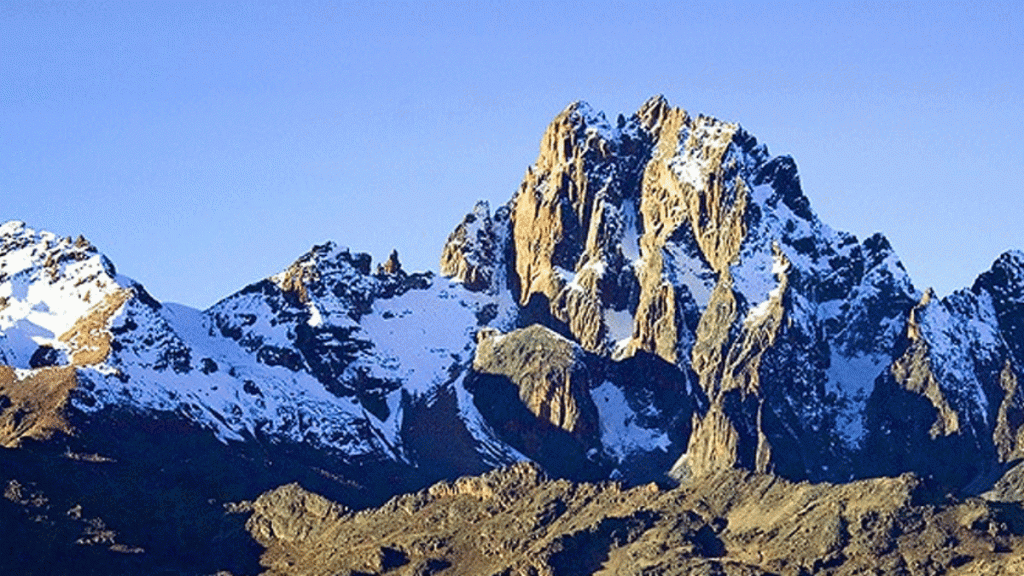 The high point of Mount Kenya, showcasing the rugged, snowy summit against a clear blue sky.