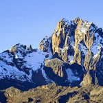 The high point of Mount Kenya, showcasing the rugged, snowy summit against a clear blue sky.