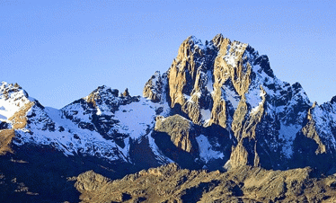 The high point of Mount Kenya, showcasing the rugged, snowy summit against a clear blue sky.